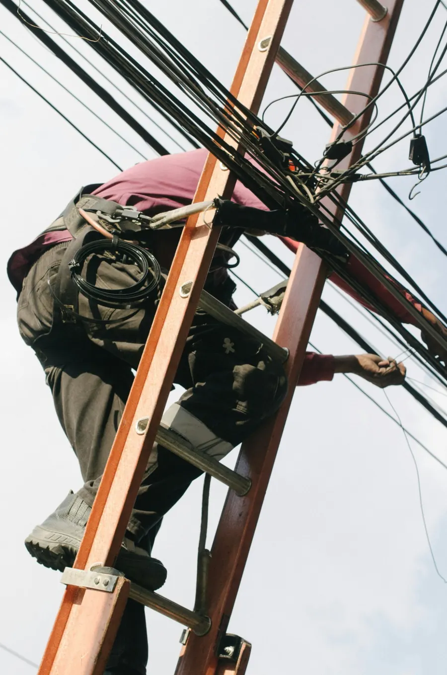 Électricien au travail sur une échelle, au milieu des câbles